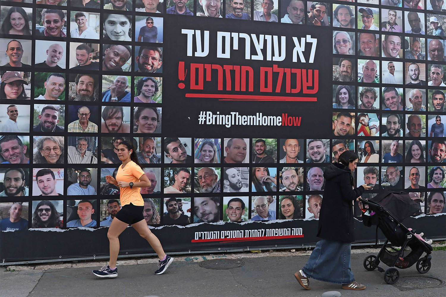 People walk past a billboard bearing the portraits of Israeli hostages, held in the Gaza Strip since the October 7, 2023 attacks by Hamas, in Jerusalem