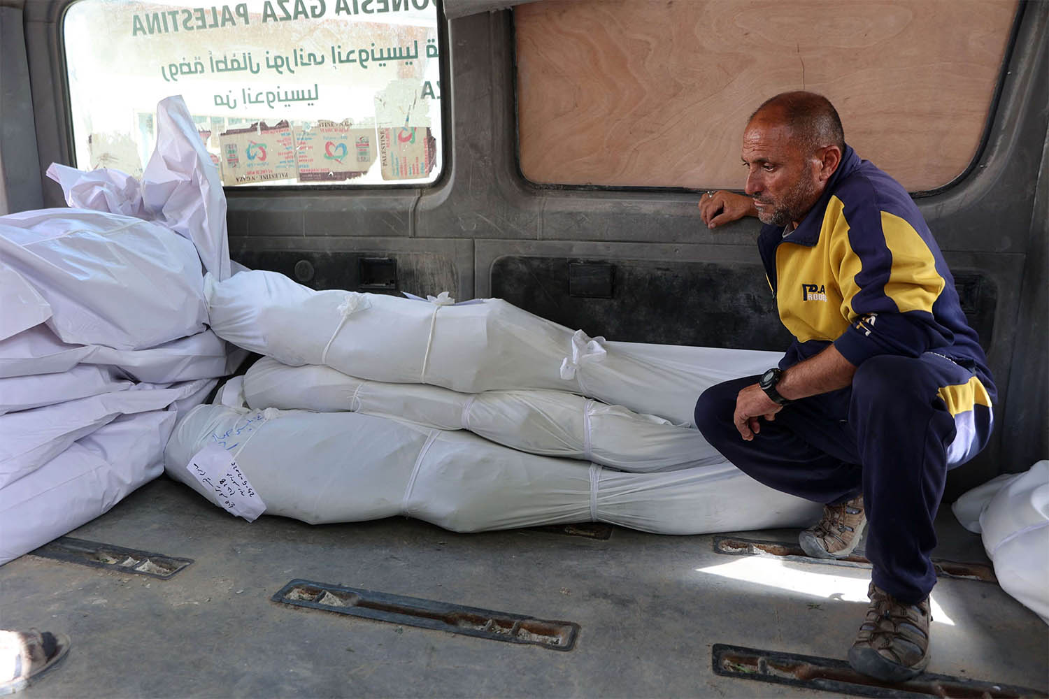 A man sits next to the shrouded bodies of people killed in the Israeli strike on the school