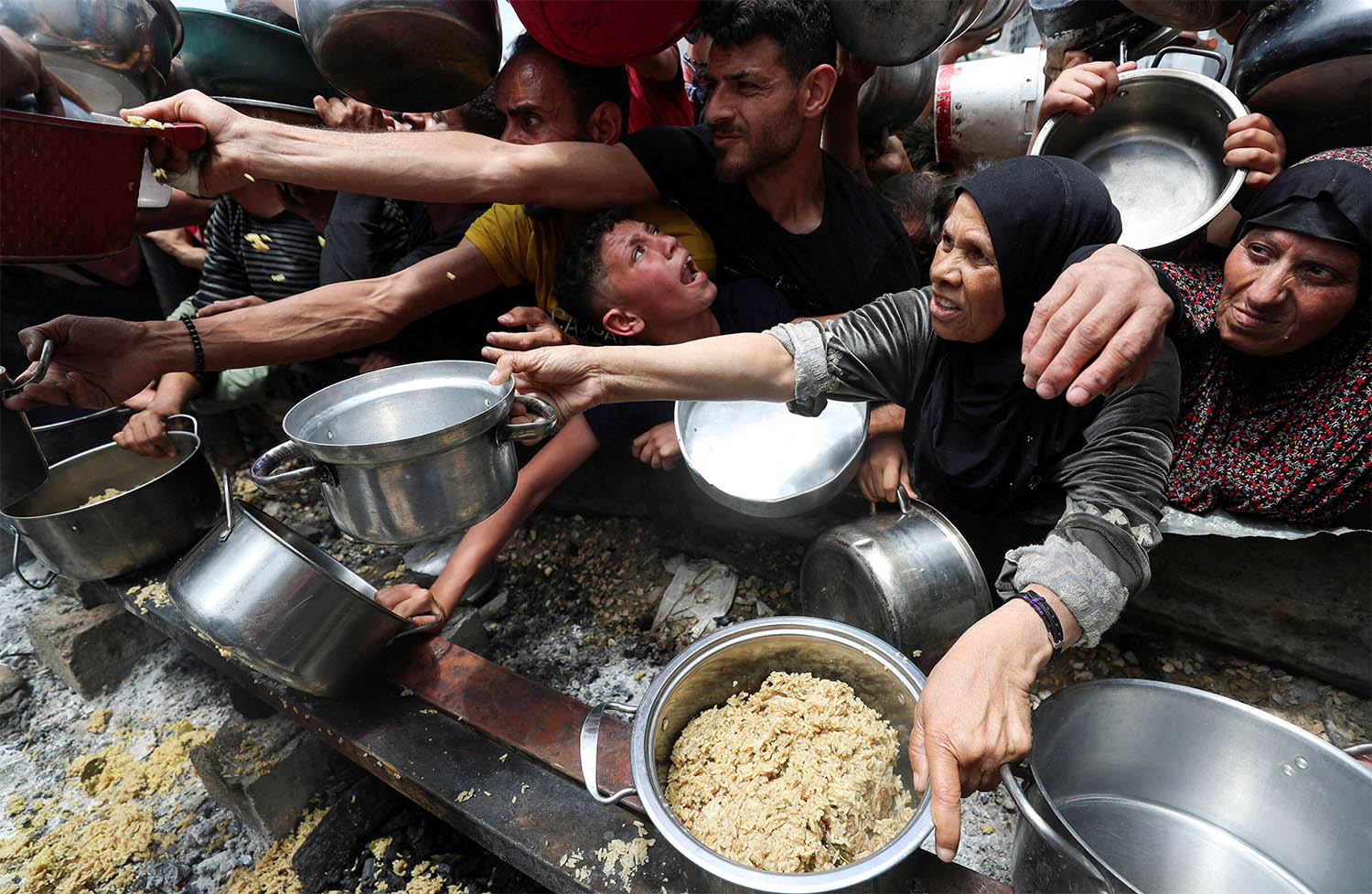 Palestinians wait to receive food cooked by a charity kitchen in Jabalia