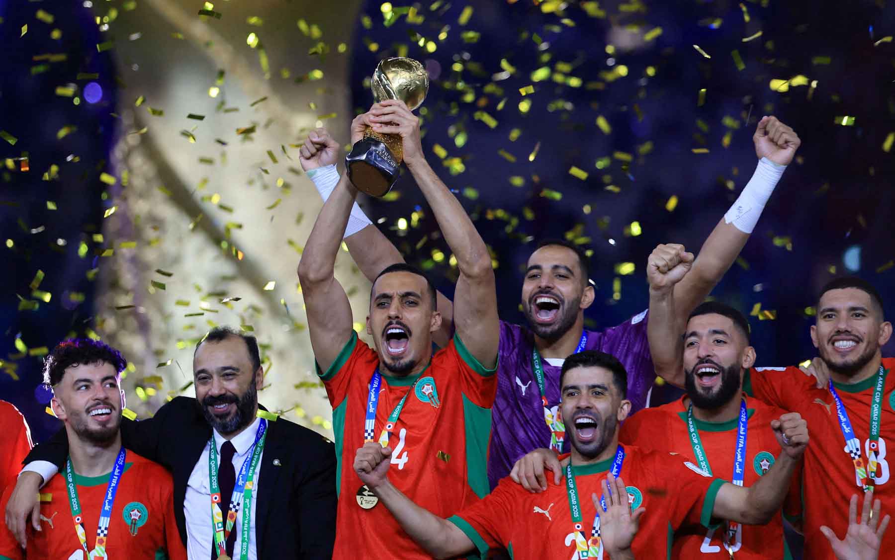 Morocco’s Soufiane Bouftini celebrates on the podium with the FIFA Arab Cup trophy along with teammates and coach Tarik Sektioui et Lusail Stadium in Qatar, December 18, 2025. 