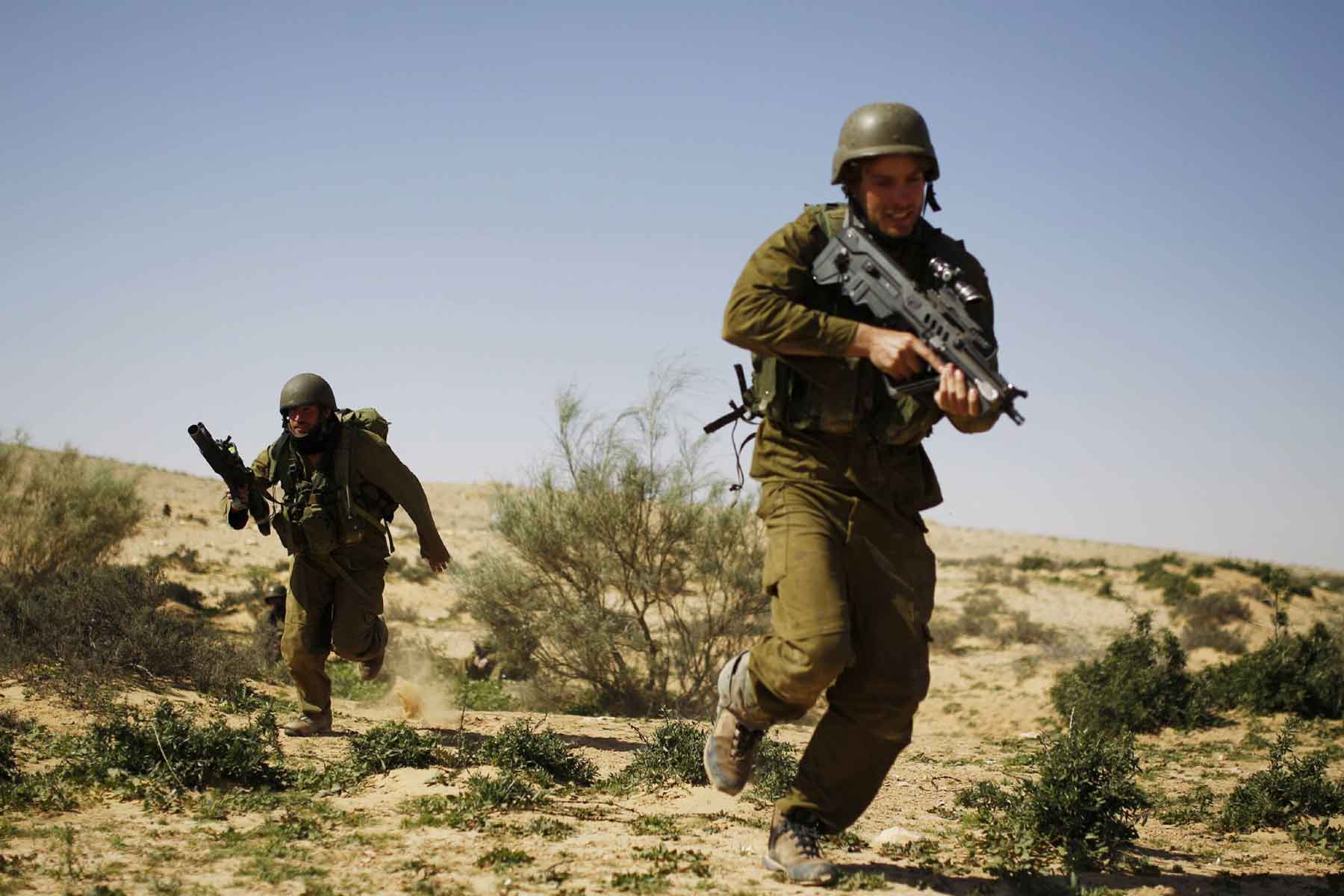Israeli reserve soldiers run with their weapons during a drill at a military zone near Kibbutz Revivim in southern Israel. 
