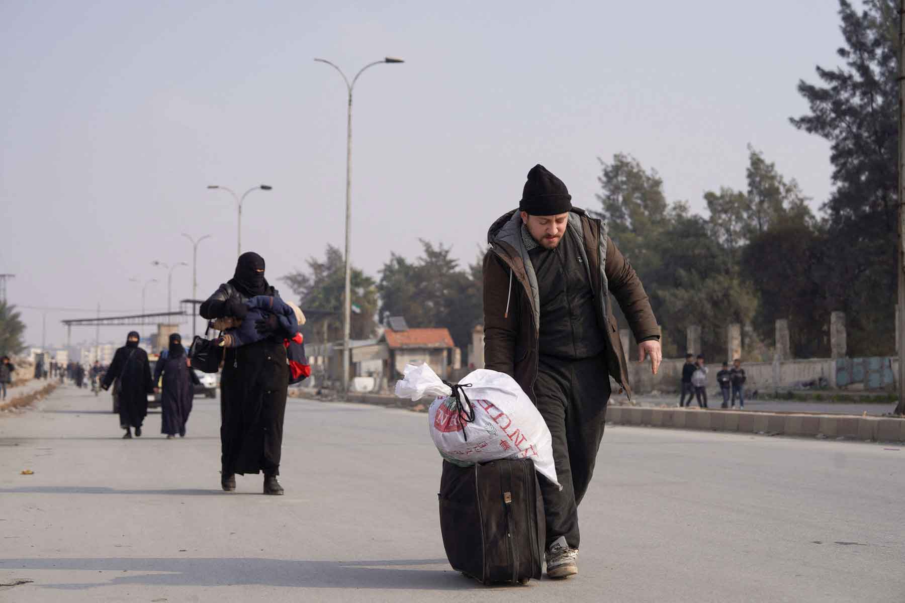 People walk with their belongings along a road, after Syrian government forces and the Kurdish-led Syrian Democratic Forces agreed to de-escalate in Aleppo, December 23, 2025. 