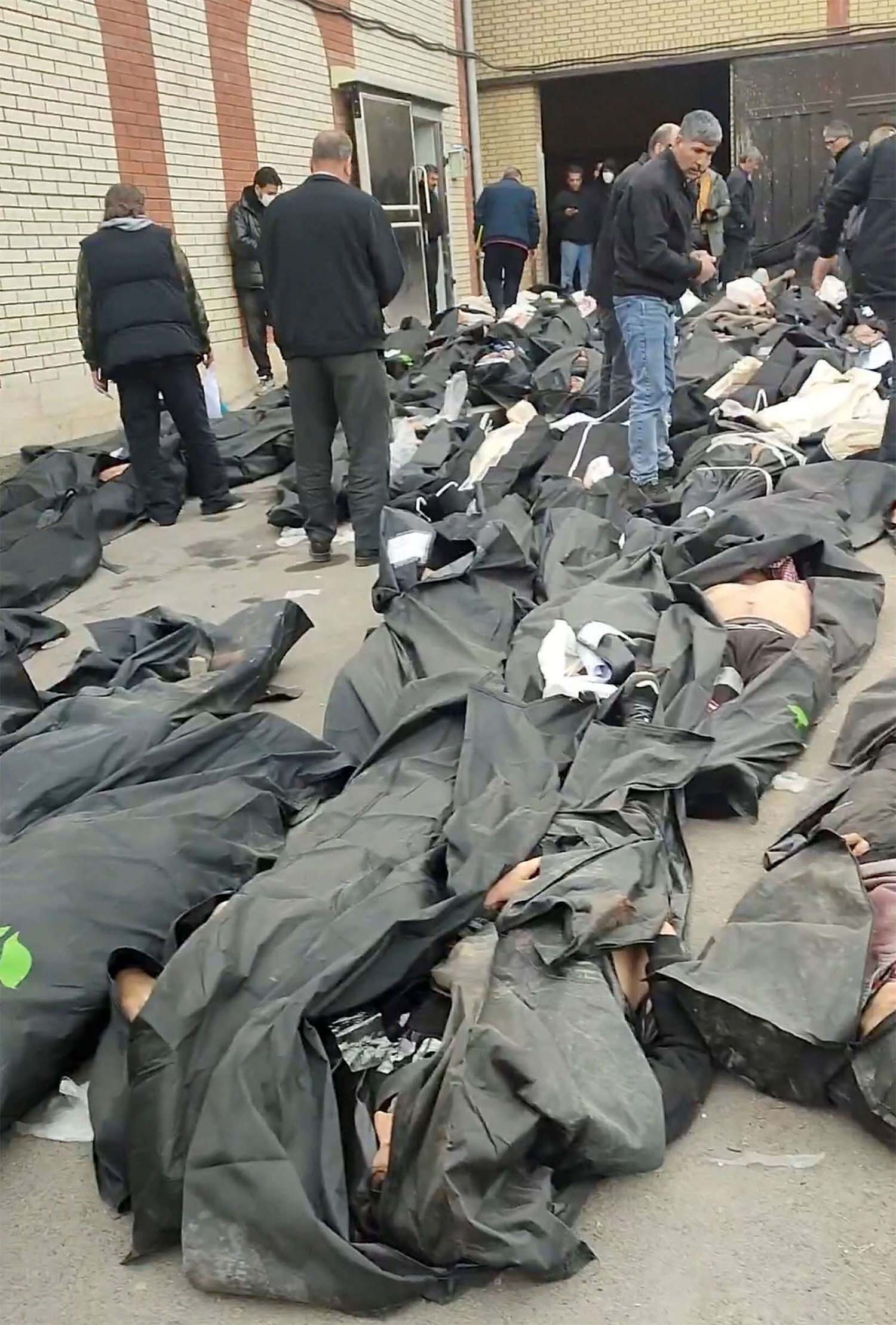 Bodies lie in body bags on the ground as people stand amid the scene outside Kahrizak Forensic Medical Centre in Tehran
