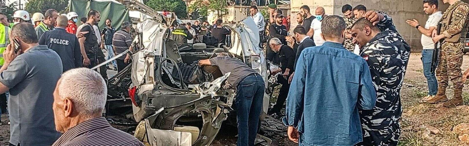 Lebanese army soldiers and onlookers gather around the carcasses of a car after it was hit by an Israeli strike