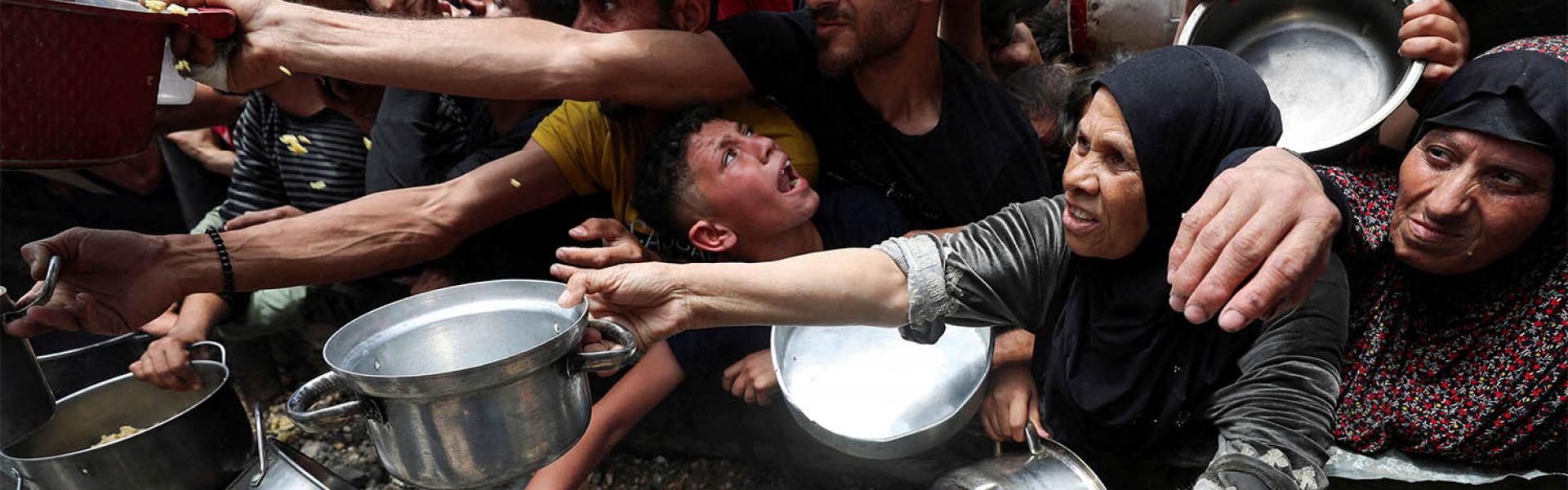 Palestinians wait to receive food cooked by a charity kitchen in Jabalia