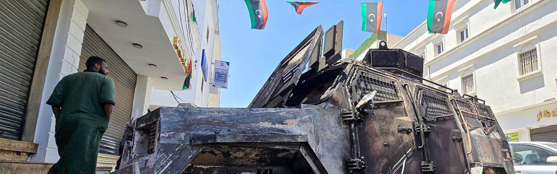 A man walks past a car that was destroyed during overnight clashes in the southern district of Abu Salim in Tripoli