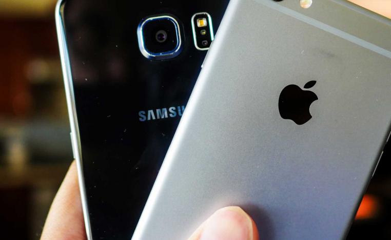 يد تمسك هاتفين احدهما لسامسونغ والاخر لآبل