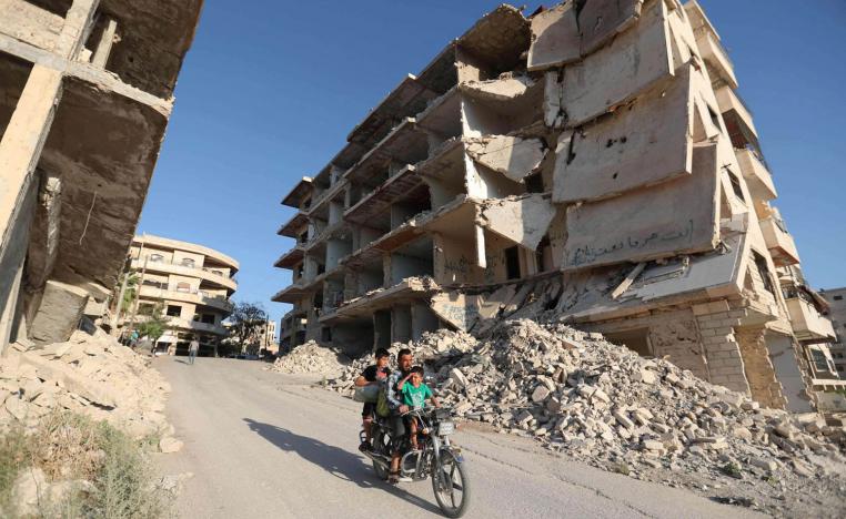 سوري يمر مع اطفاله بالقرب من أبنية مدمرة في معرة النعمان