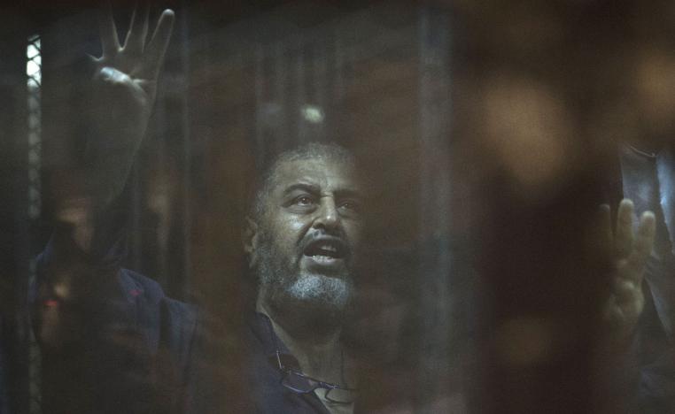 Egyptian Muslim Brotherhood financier Khairat al-Shater gestures from behind the defendant's cage as he attends his trial in Cairo on June 16, 2015. 