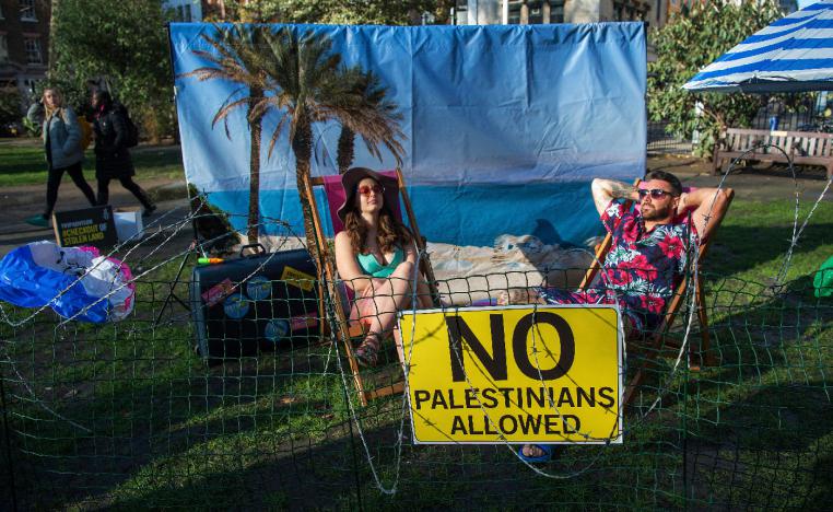 Two models sit on a "barbed-wire beach" outside the offices of TripAdvisor in Soho Square, as part of an Amnesty International campaign calling on the firm and other travel companies to stop listing rooms and activities in Israeli settlements in the Palestinian Territories on 30 January 2019 in London, England.