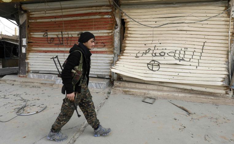 A fighter from the Syrian Democratic Forces (SDF) walks past shops with their fronts painted with the Arabic phrases "beware a sniper" and "caliphate state", in the city of Hajin in Syria's eastern Deir Ezzor province on January 27, 2019.