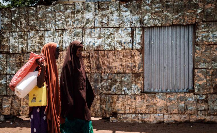 Women walk in front of a metal fence made of vegetable oil cans from USAID at the Dadaab refugee complex, northeastern Kenya, on April 18, 2018.