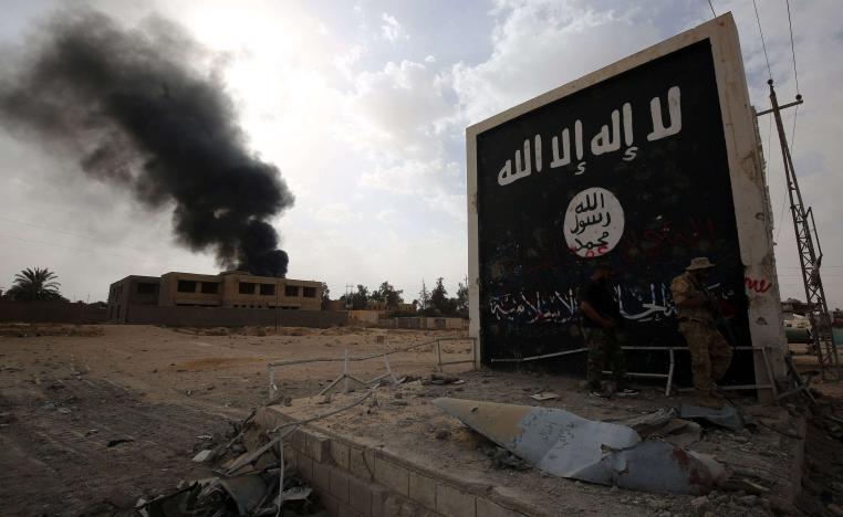 Iraqi fighters of the Hashed al-Shaabi (Popular Mobilisation units) stand next to a wall bearing the Islamic State (IS) group flag as they enter the city of al-Qaim, in Iraq's western Anbar province near the Syrian border as they fight against remnant pockets of Islamic State group jihadists on November 3, 2017.
