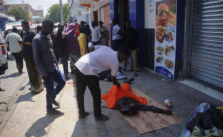 Somalis examine the dead body of a civilian killed after an explosion outside a restaurant