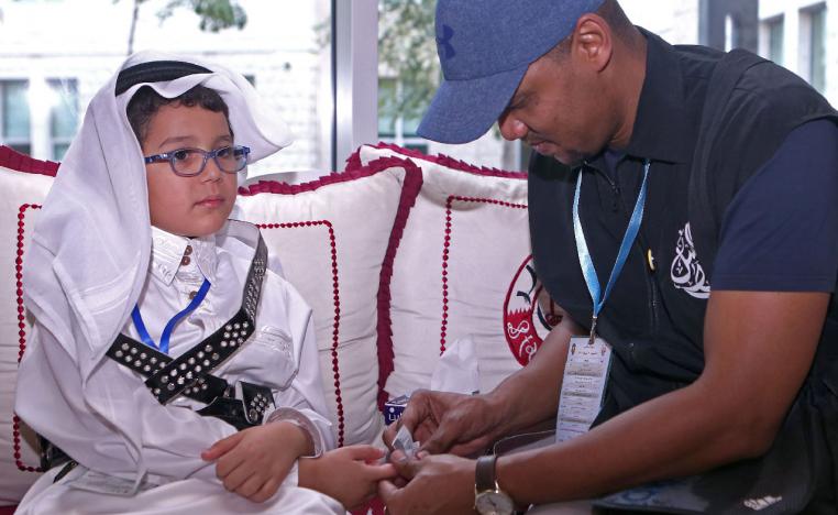 A man tests Qatari child Tamim Abdelmoniem Allafi's blood during the 19th International al-Bawasil Children with diabetes camp in Doha.
