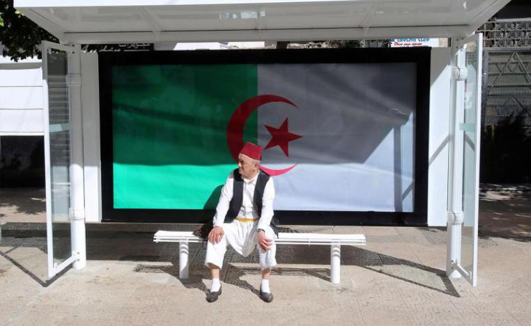 A man sits at a bus station decorated with the national flag in Algiers