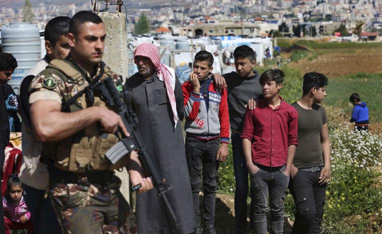 A Lebanese army soldier stand guards in front of Syrian refugees who stand outside their tent to watch the opening ceremony of a school for Syrian refugees, in the Bekaa valley