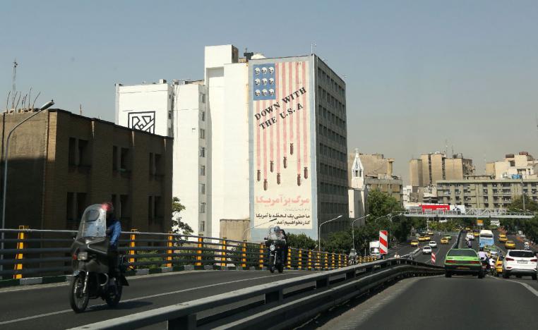Cars drive past mural painting along the wall of a building in the Iranian capital Tehran