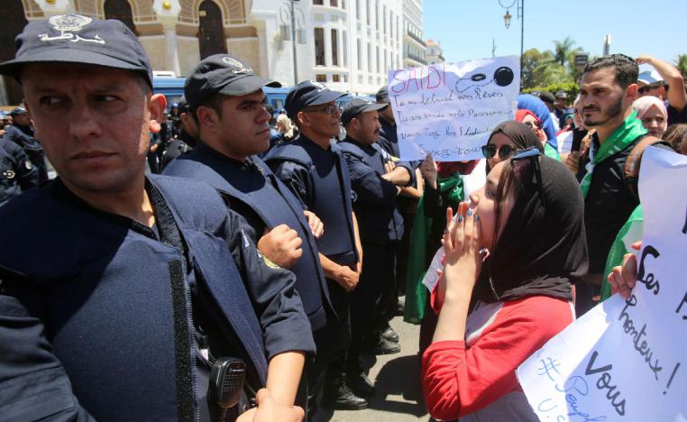 Police officers stand guard as students chant slogans during a protest demanding the removal of the ruling elite in Algiers