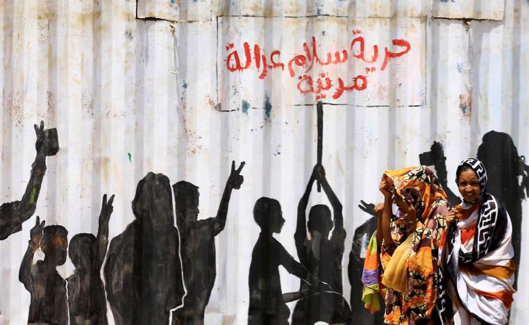 Civilians walk past graffiti reading in Arabic "Freedom, Peace, Justice and Civilian" in the Burri district of Khartoum