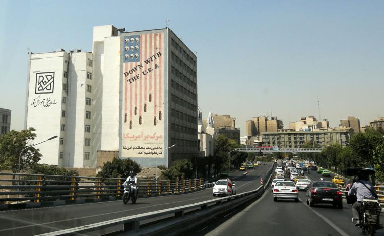 Cars drive past a mural painted on the wall of a building showing an anti US slogan in the capital Tehran