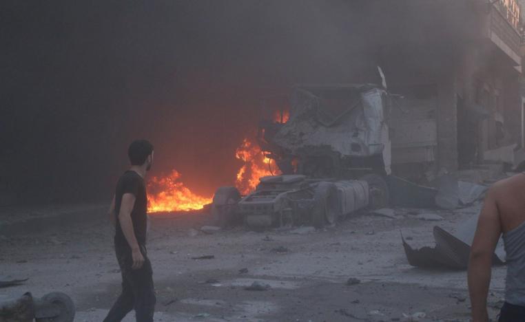 People walk next to fire, debris and a damaged truck after a deadly airstrike in Idlib province