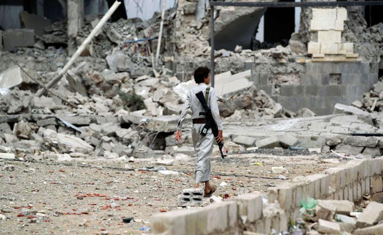 Huthi militant walks amidst the debris of a house