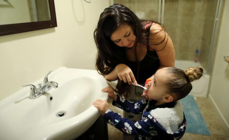 أم تساعد طفلتها في تنظيف أسنانها بالفرشاة والمعجون