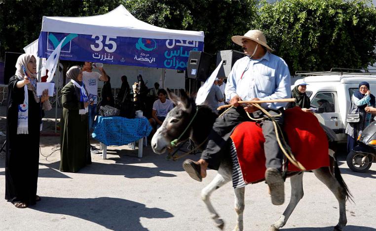 A man rides a donkey past a campaign stall of Tunisia's moderate Islamist Ennahda party in al-Alia