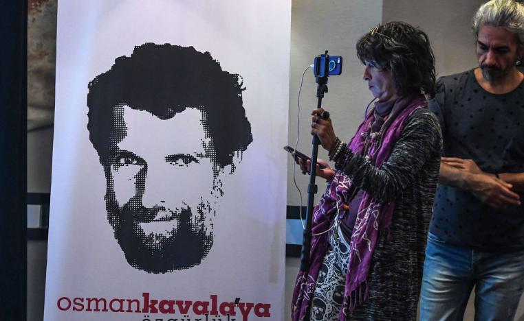 A journalist stands in front of a poster featuring jailed businessman and philanthropist Osman Kavala