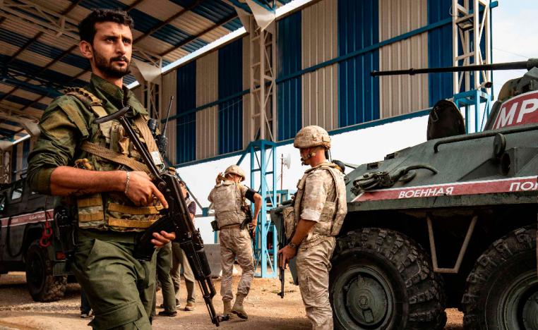 A member (L) of the Syrian Kurdish Asayish internal security forces walks past Russian military police members