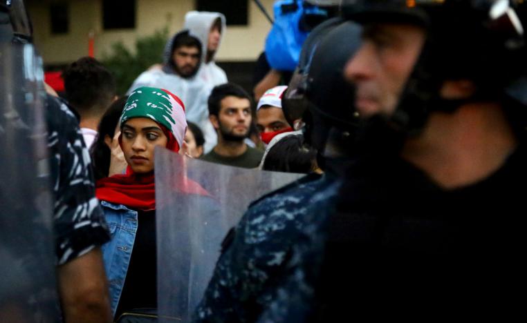 A demonstrator stands behind riot police during a protest at Riad al-Solh square in Beirut