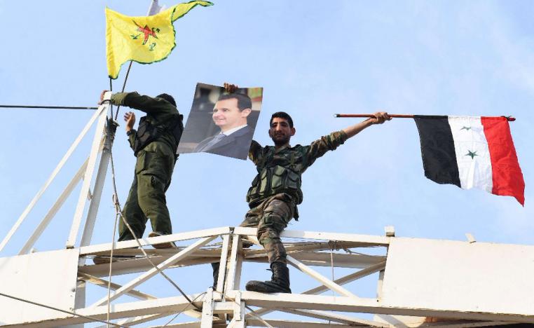 A Syrian government soldier holds up a portrait of President Bashar al-Assad and a Syrian national flag while another stands by a Kurdish YPG flag