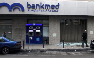 Men walk near broken glass from a damaged Bankmed branch in Tripoli, Lebanon