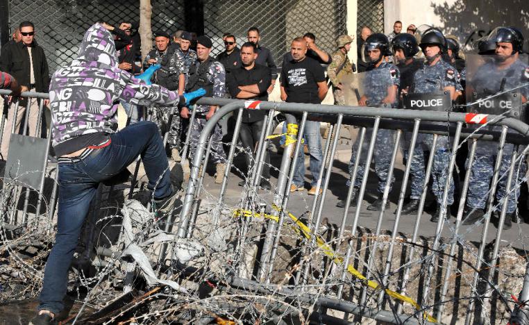 A Lebanese protester steps on a metal barrier through a barbed wire fence near the parliament headquarters in Beirut