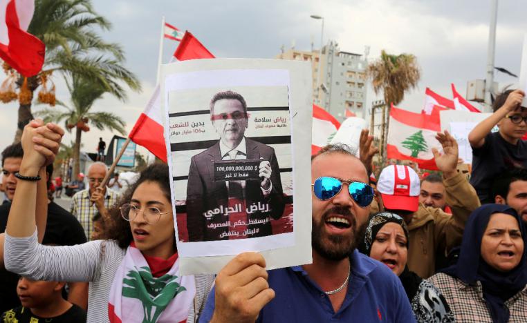 Demonstrators carry Lebanese flags and a banner depicting Lebanon's Central Bank Governor Riad Salameh