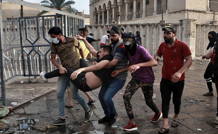 عراقيون يحملون زميلهم الجريح بعد استهدافه من فبل قوات الأمن