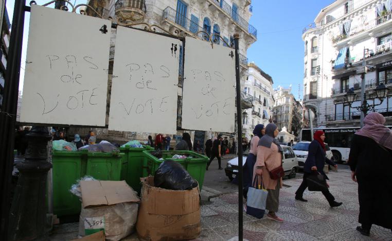 "No vote" reads on electoral panels as women walk past in Algiers