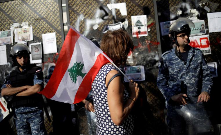 A protester holds a Lebanese flag as she walks in front of police officers