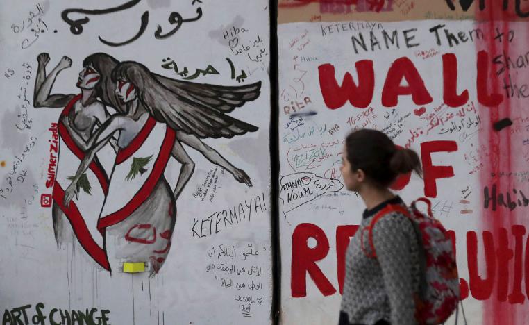 لبنانية تمر بجانب غرافيتي عن الثورة في لبنان