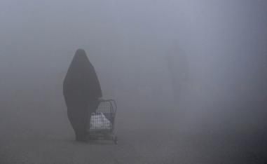 عراقية تمشي وسط الضباب في بغداد
