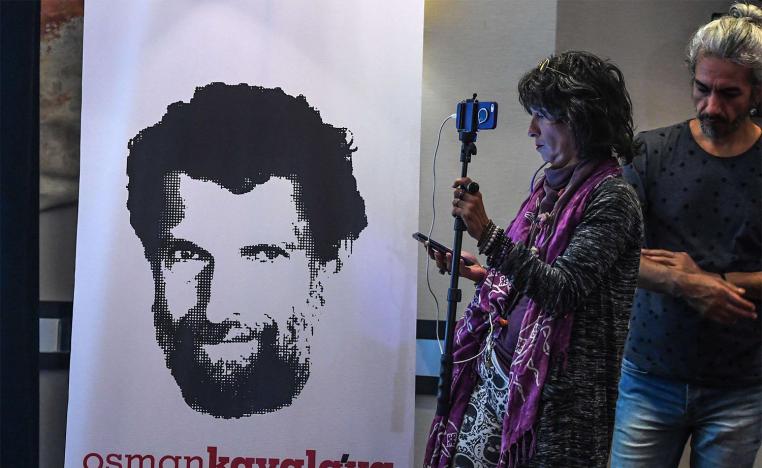 A journalist stands in front of a poster featuring businessman and philanthropist Osman Kavala