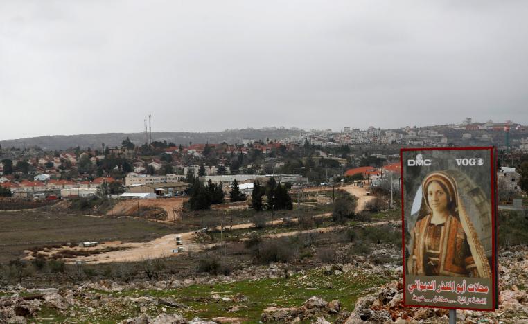 A sign for a Palestinian clothing shop is seen in the village of Silwad as the Jewish settlement of Ofra appears in the background