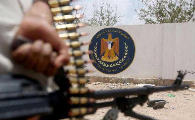 A Yemeni government soldier holds a weapon as he stands by an emblem of the Southern Transitional Council