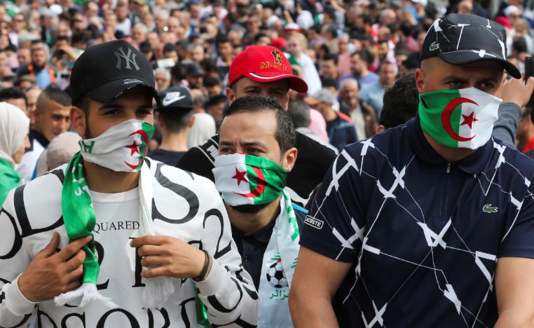 Demonstrators cover their faces with national flags during an anti-government protest in Algiers