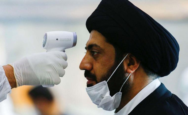 A medical staff member in protective gear checks the temperature of a cleric man amid concerns over the coronavirus (COVID-19) spread at Najaf airport