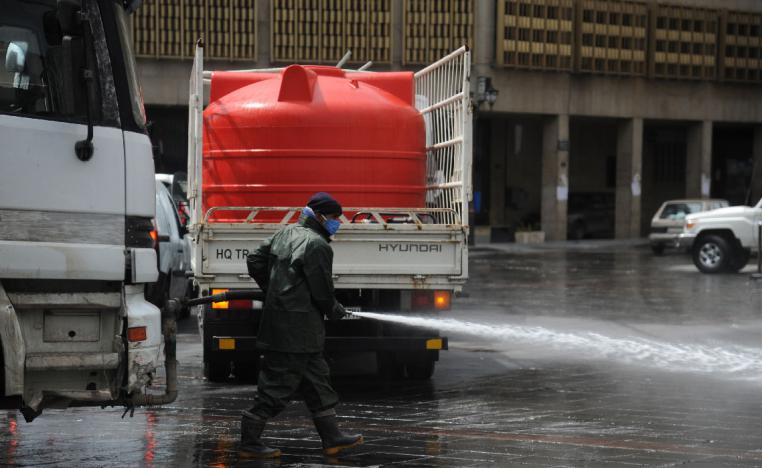 A Syrian worker wearing a protective face mask cleans a street