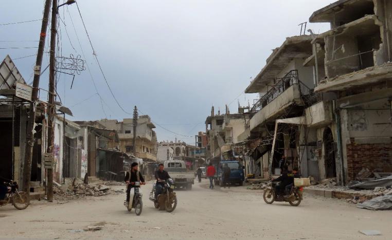 Syrian men ride their motorcycles through a damaged neighbourhood in the town of Binnish