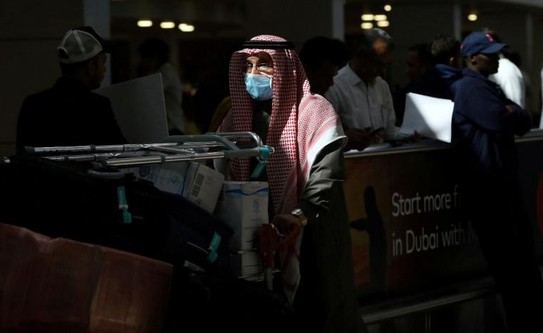 A traveller wears a mask as he pushes a cart with luggage at Dubai International Airport
