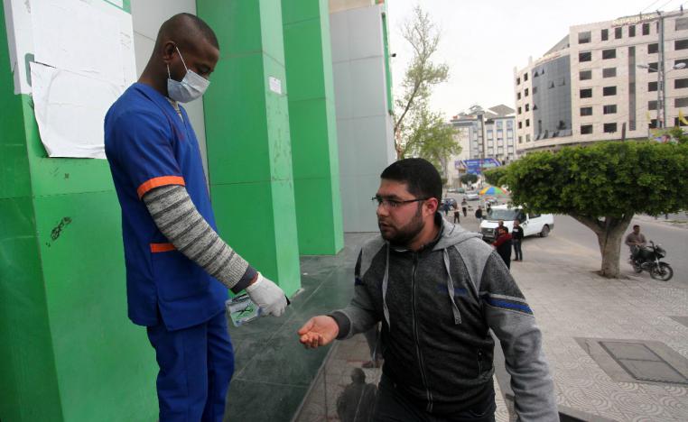 A worker sprays disinfectant on the hands of a Palestinian man at a Post Office in Gaza
